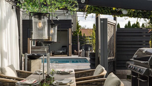 An outdoor dining area with wicker chairs, a pool, and a grill.
