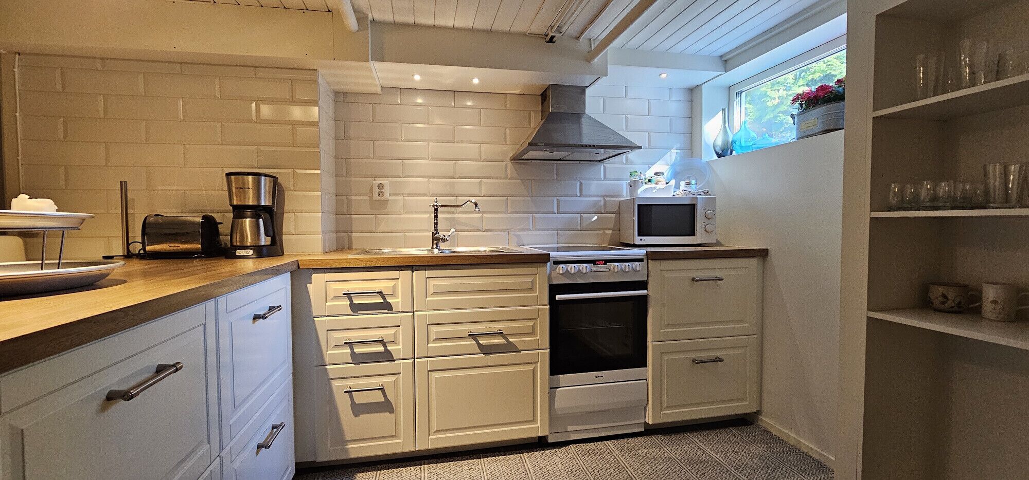 A compact kitchen with white cabinetry, a coffee maker, a microwave, and a stove.