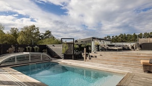 A pool with a wooden deck, a barbecue area, and a covered seating area.