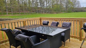 Une terrasse dotée d’une table à plateau en verre et de quatre chaises, d’un barbecue et d’une rambarde en bois.