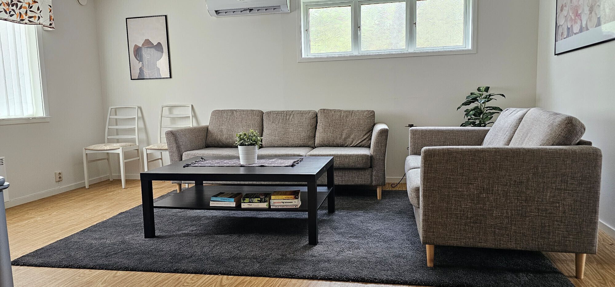 A living room with a sofa, armchair, and coffee table. There is a plant on the coffee table and a window with blinds.