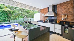 A modern kitchen with a central island, a built-in oven, and a dishwasher. - Casa Riviera 292 (Bertioga)