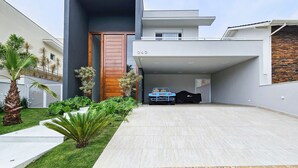 A modern house with a garage, a well-maintained lawn, and a blue toy car. - Casa Riviera 292 (Bertioga)