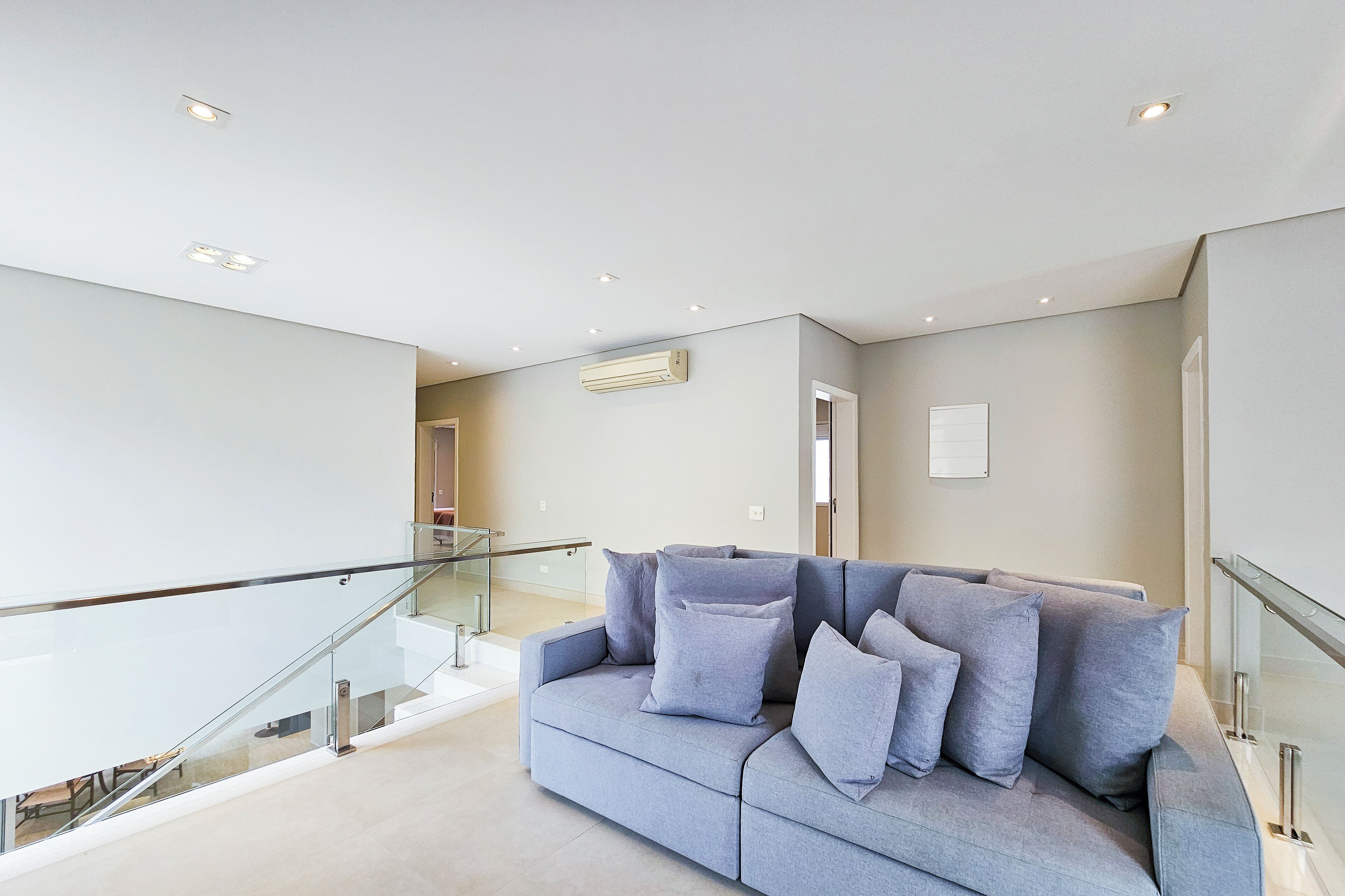 A modern living room with a grey sofa, glass railings, and recessed ceiling lighting.