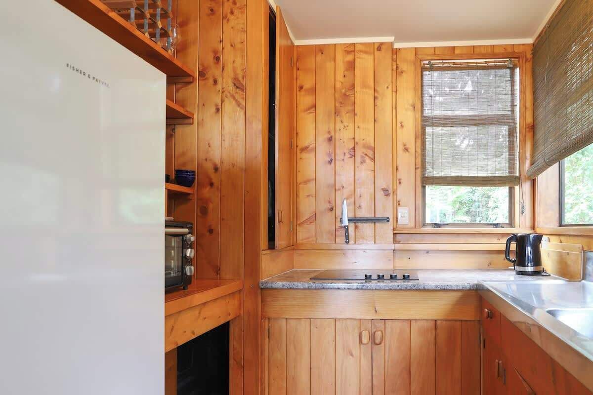Een houten keuken met een ingebouwde oven, een spoelbak en een raam met jaloezieën.