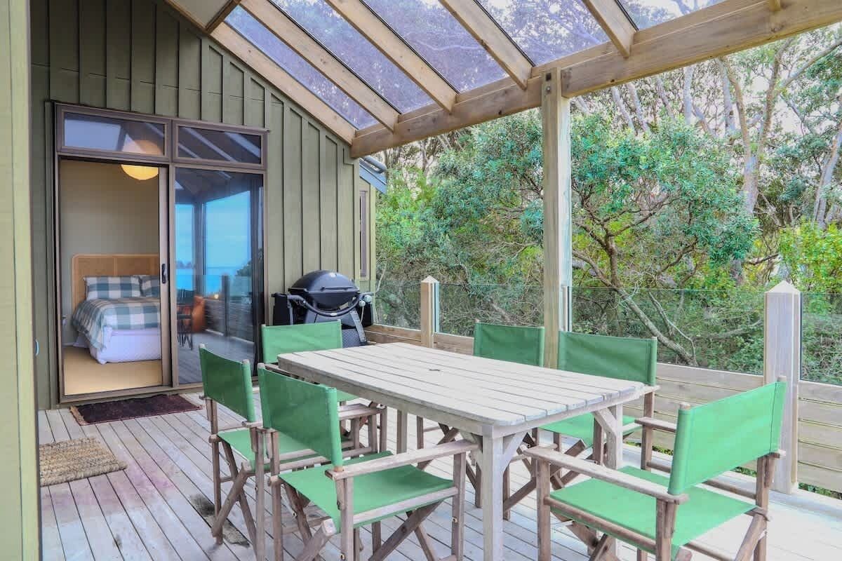 Ein überdachter Außenbereich mit Tisch und Stühlen, eine Glastür zum Schlafzimmer hin und ein Grill.