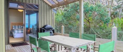 Ein überdachter Außenbereich mit Tisch und Stühlen, eine Glastür zum Schlafzimmer hin und ein Grill.