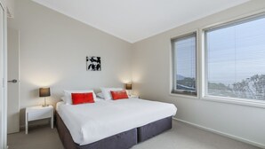 A bedroom with a bed, two bedside tables, a nightstand, a wall art piece, and a window with blinds.
