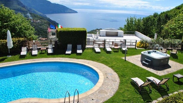 A pool area with lounge chairs and a hot tub, surrounded by a well-maintained lawn and a scenic view of the sea and mountains. - B&B Villa La Ventana (Sant'Agnello)