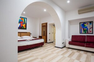 A hotel room with a bed, a red sofa, and two abstract paintings on the walls.