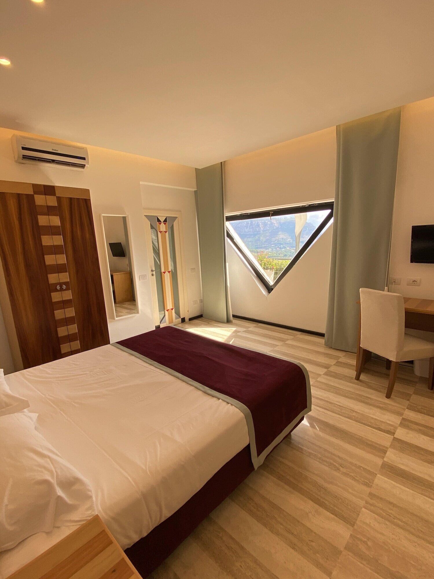 A modern hotel room with a large bed, a desk, and a window with a mountain view.
