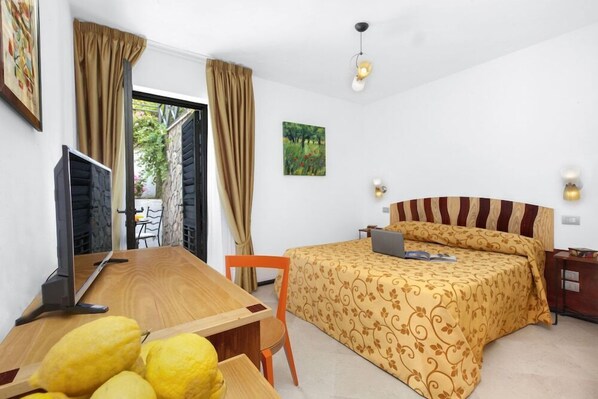 Un dormitorio con cama, escritorio con computadora y silla. Se ve una ventana con cortinas, un cuadro en la pared y una lámpara en la mesita de noche.