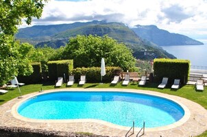 Piscina con sillas de descanso y vistas a las montañas y al mar.