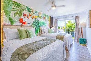 Habitación de hotel con dos camas, un mural tropical grande, un balcón con vistas y un ventilador de techo.