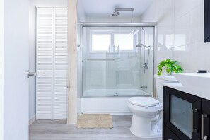 Un baño moderno con ducha de vidrio, inodoro blanco y un mueble negro.