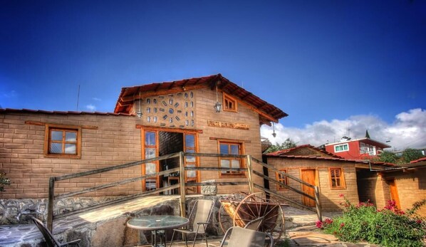 A wooden building with a staircase leading to a door, a small table with chairs, and a wheelbarrow. - Hotel Finca Belen  (Tlaxco)