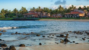 Un hotel frente a la playa con varias edificaciones, palmeras y un litoral rocoso.