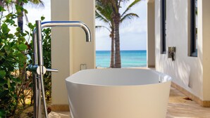 A white bathtub in a room with a view of the ocean and palm trees.