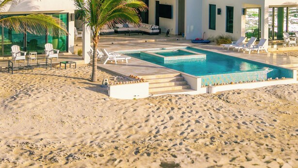 A beachfront property with a swimming pool, lounge chairs, and a covered patio area.