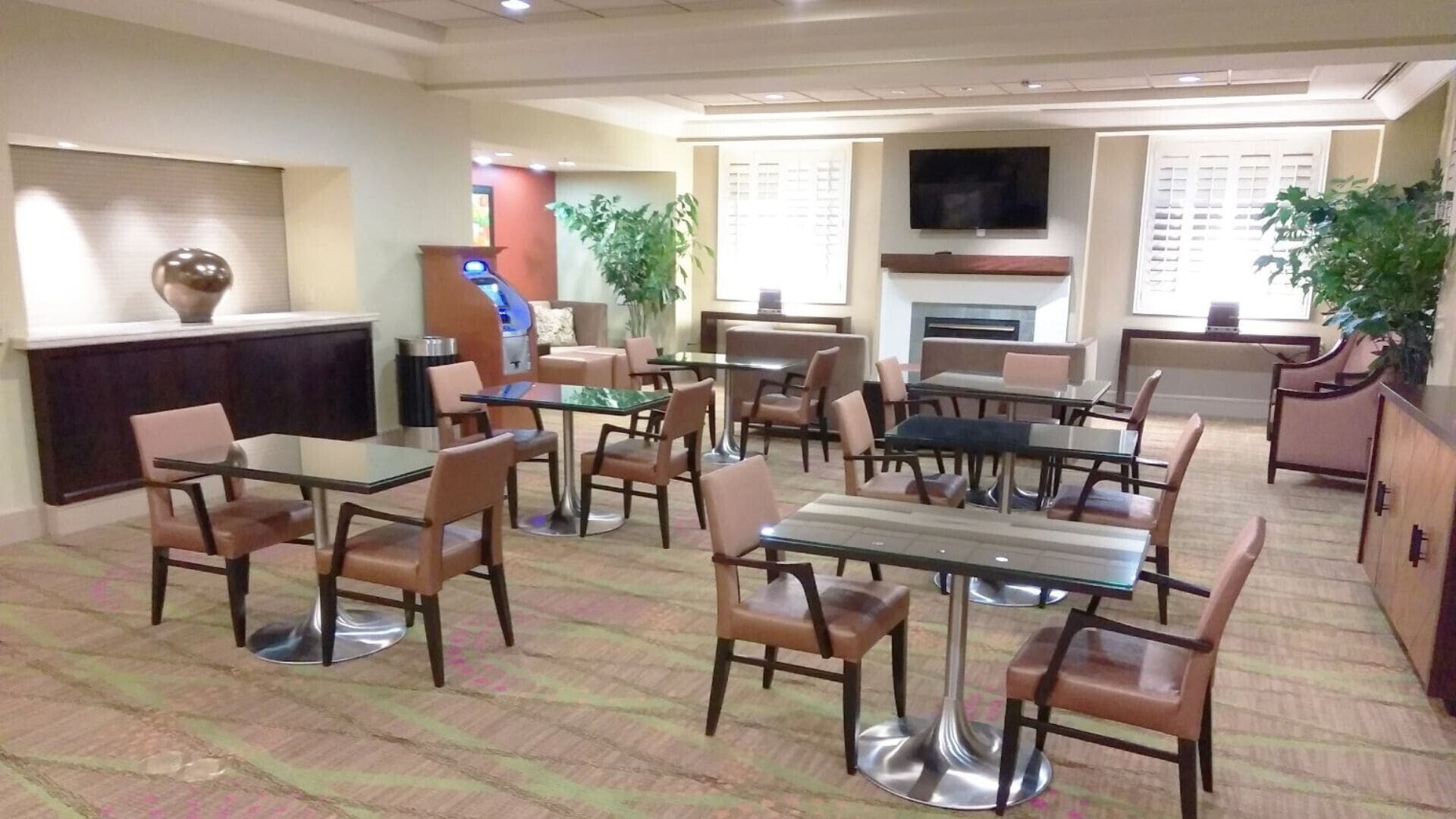 Une salle à manger d’hôtel avec plusieurs tables et chaises, une cheminée et un téléviseur fixé au mur.