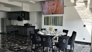 A modern dining area with a round table set for six, surrounded by black upholstered chairs with circular cutouts. A large flat-screen TV is mounted on the wall above the table. - Spacious 4-bedroom apartment with WiFi, AC in fantastic LUXURY (Tambon Patong)