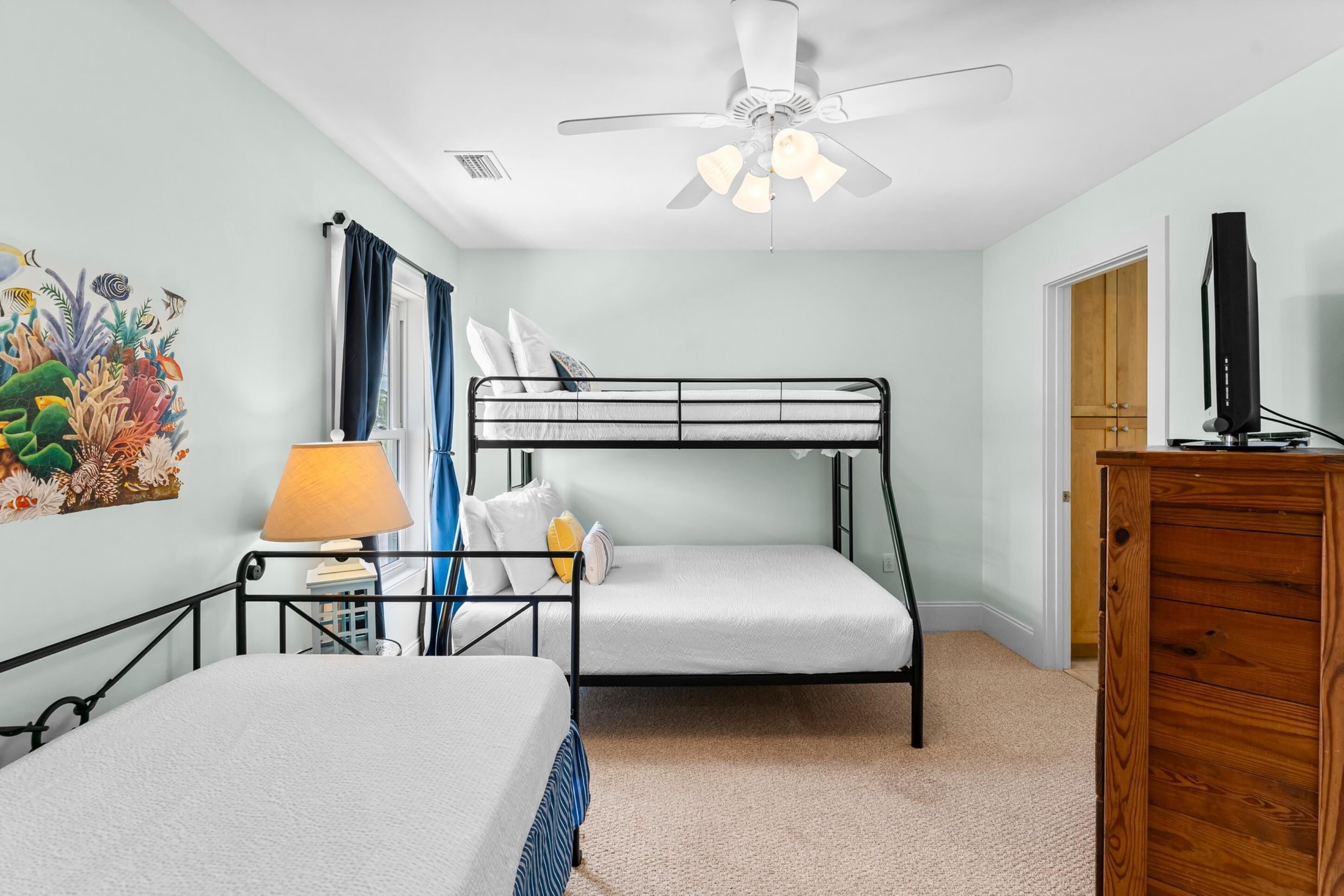A bedroom with bunk beds, a ceiling fan, a lamp, a dresser, and a wall painting.