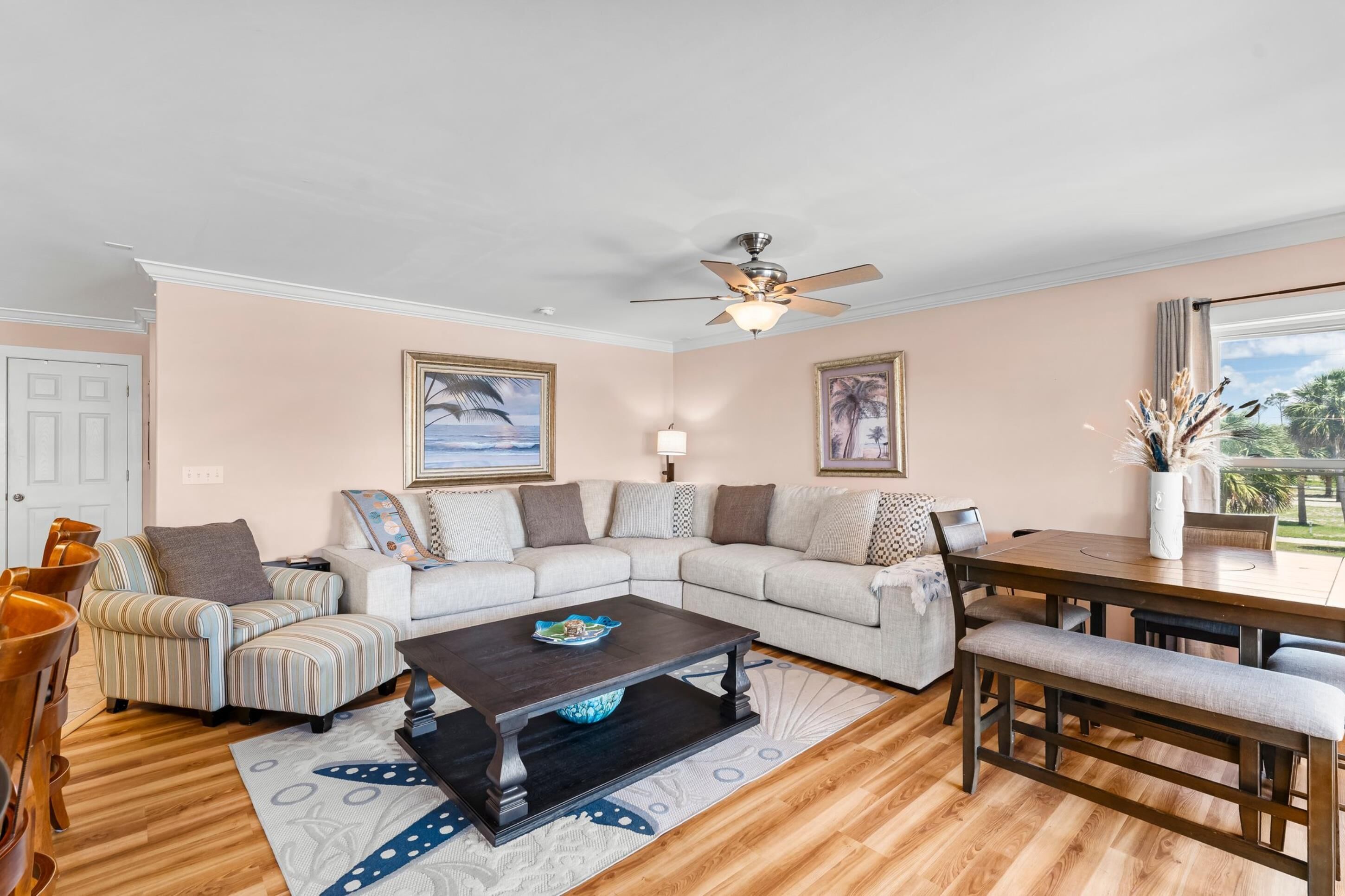 A living room with a sectional sofa, a coffee table, a dining table with chairs, a ceiling fan, and framed artwork on the walls.