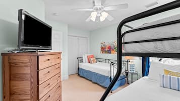 Un dormitorio con una cama litera, un aparador de madera, un televisor, un ventilador de techo y un cuadro llamativo en la pared.