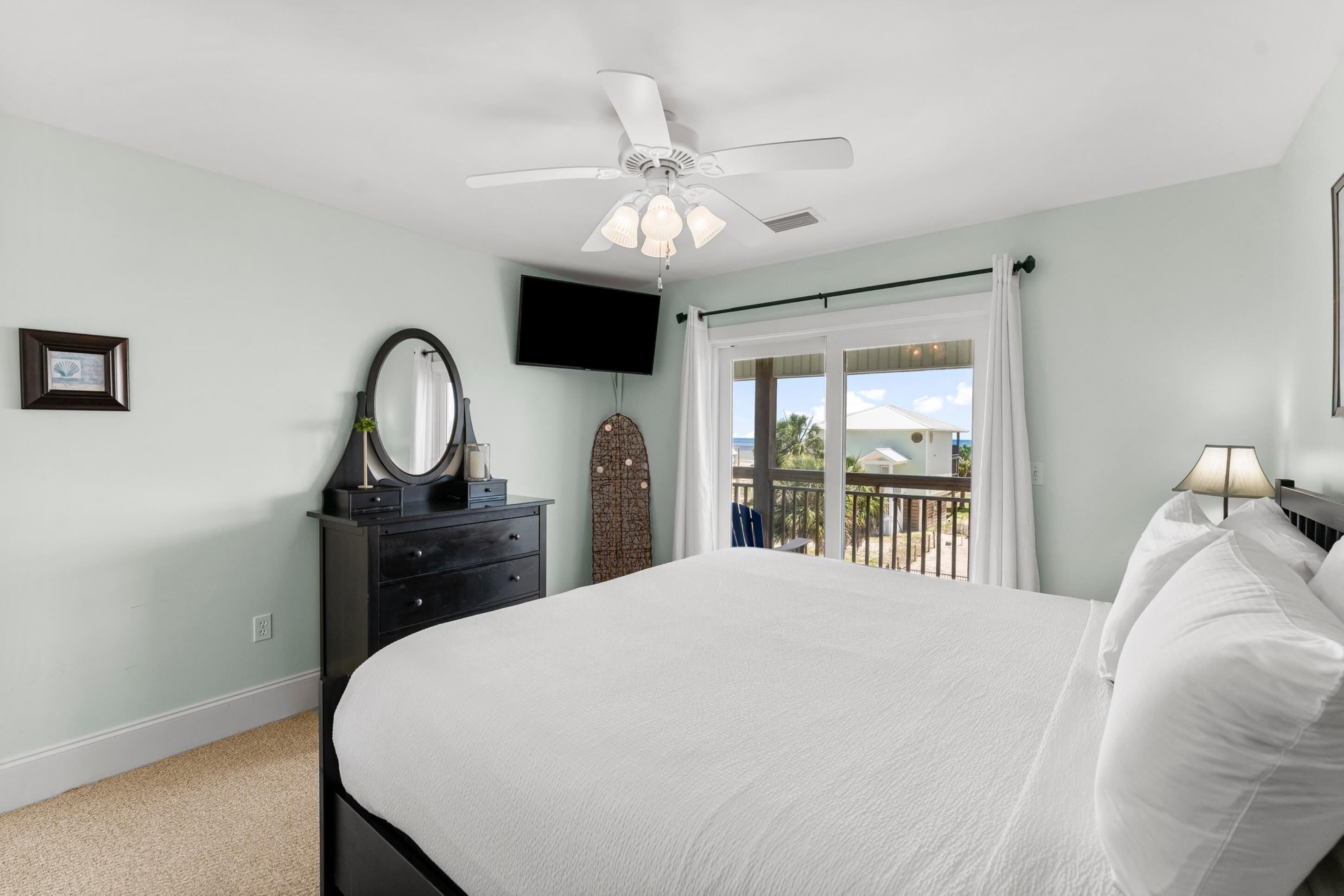 Un dormitorio con cama, ventilador de techo, cómoda, televisor y balcón con vistas.