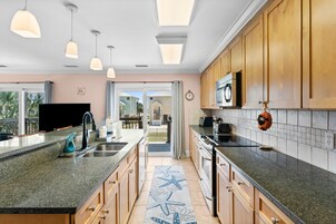 Une cuisine moderne dotée de plans de travail en granit, d’armoires en bois et de luminaires suspendus.