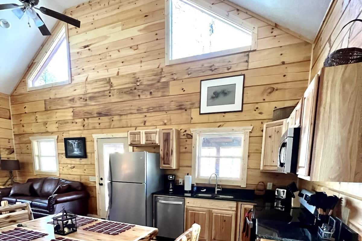 A cozy cabin-style kitchen with wooden walls, a dining table, and a refrigerator.