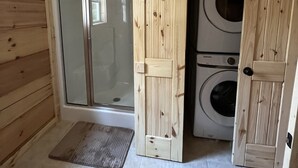 Ett litet, kompakt rum med dusch, tvättmaskin och en dörr av trä.