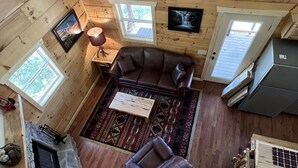 En stuga med träpanel i taket, en steneldstad, en brun lädersoffa, ett träbord och en mönstrad matta.