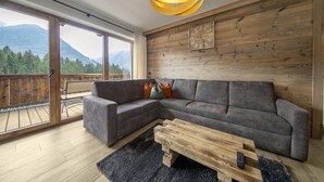 A modern living room with a large sectional sofa, a wooden coffee table, and a view of mountains through large windows. - Chalet in Neukirchen for 8 People (Neukirchen am Grossvenediger)