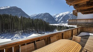 A wooden deck with a view of snow-covered mountains and pine trees. - Chalet in Neukirchen for 8 People (Neukirchen am Grossvenediger)