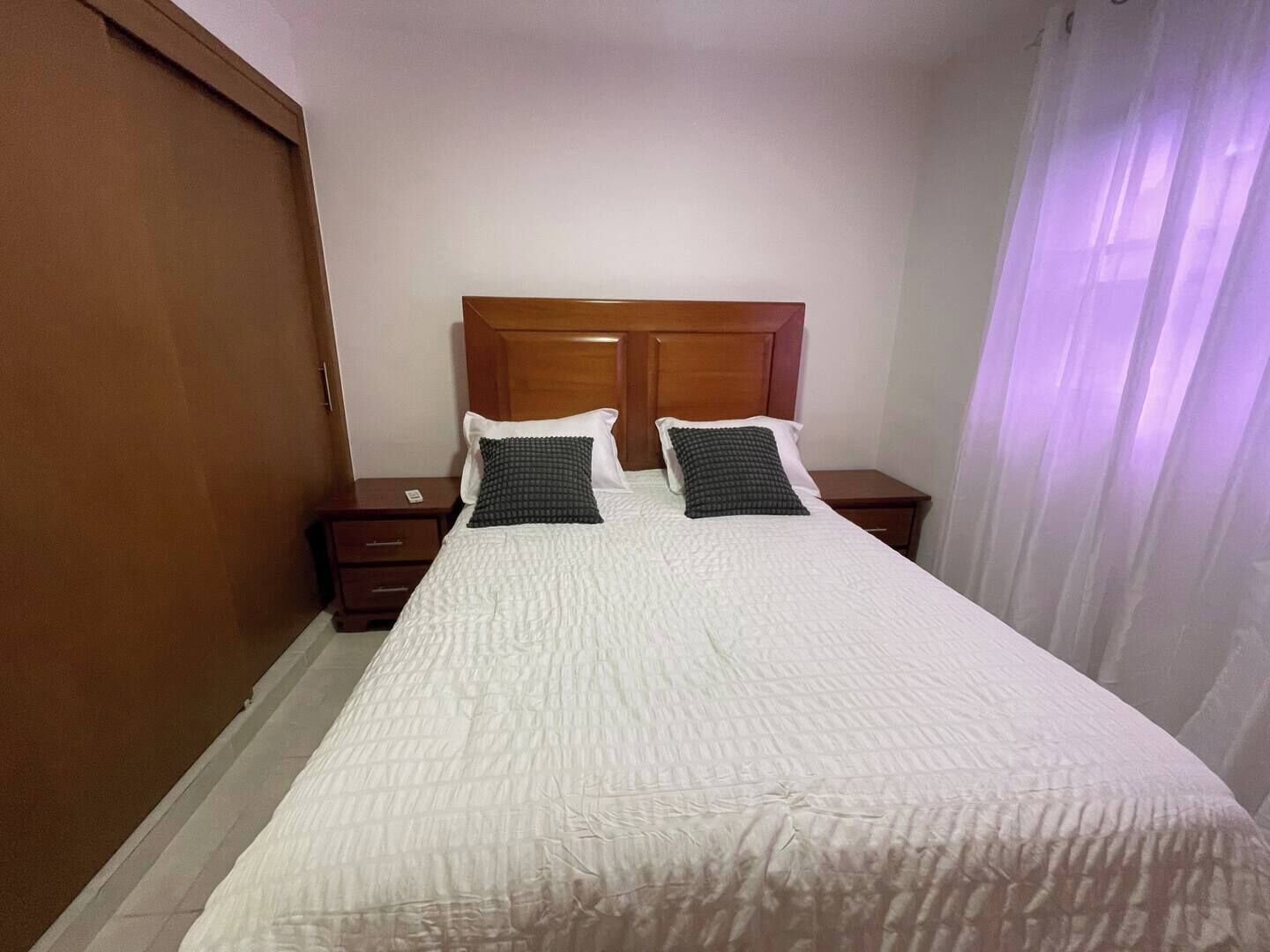 Un lit bien fait, avec une couette blanche, deux oreillers et une tête de lit en bois.