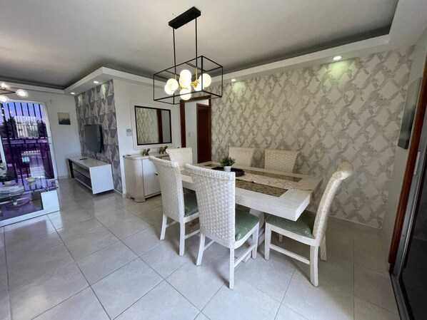Un comedor moderno con una mesa rectangular, sillas blancas y una lámpara de techo con diseño geométrico.