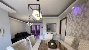 Un comedor con una larga mesa, sillas acolchadas, una planta central e iluminación colgante.