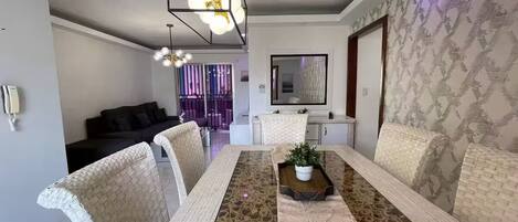 A dining area with a long table, cushioned chairs, a central plant, and pendant lighting.