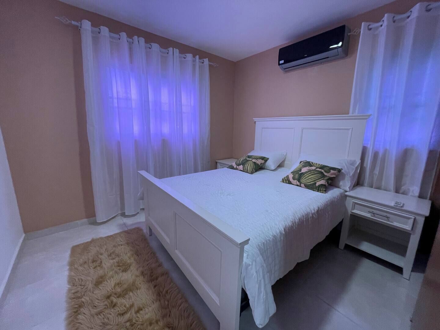 Un dormitorio con cama, mesitas de noche, una alfombra mullida y un aire acondicionado de pared.