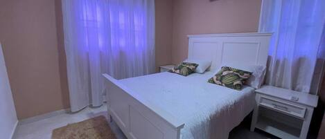 Un dormitorio con cama, mesitas de noche, una alfombra mullida y un aire acondicionado de pared.