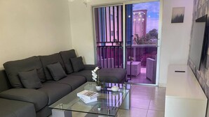 Un salón moderno con un sofá gris oscuro, una mesa de centro de vidrio y un armario blanco.