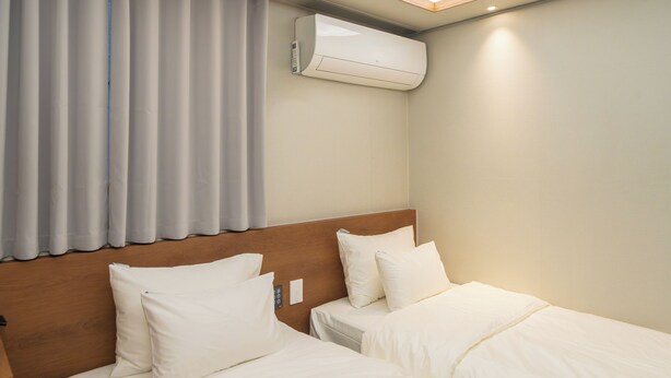 Habitación de hotel con dos camas, aire acondicionado instalado en el techo y una ventana con cortinas.