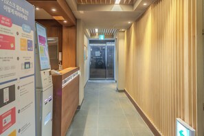 A hotel reception area with a reception desk, a digital information board, and a glass elevator. - The Square Hostel Jongno (Seoul)
