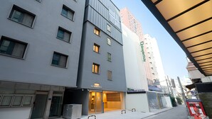 Un edificio moderno de varios pisos, con entrada visible y un cartel que indica 'The Square Hotel'.