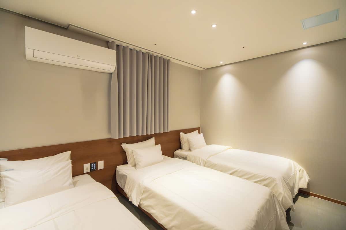 Une chambre d’hôtel avec deux lits, une tête de lit en bois, un appareil de climatisation et une fenêtre avec des rideaux.