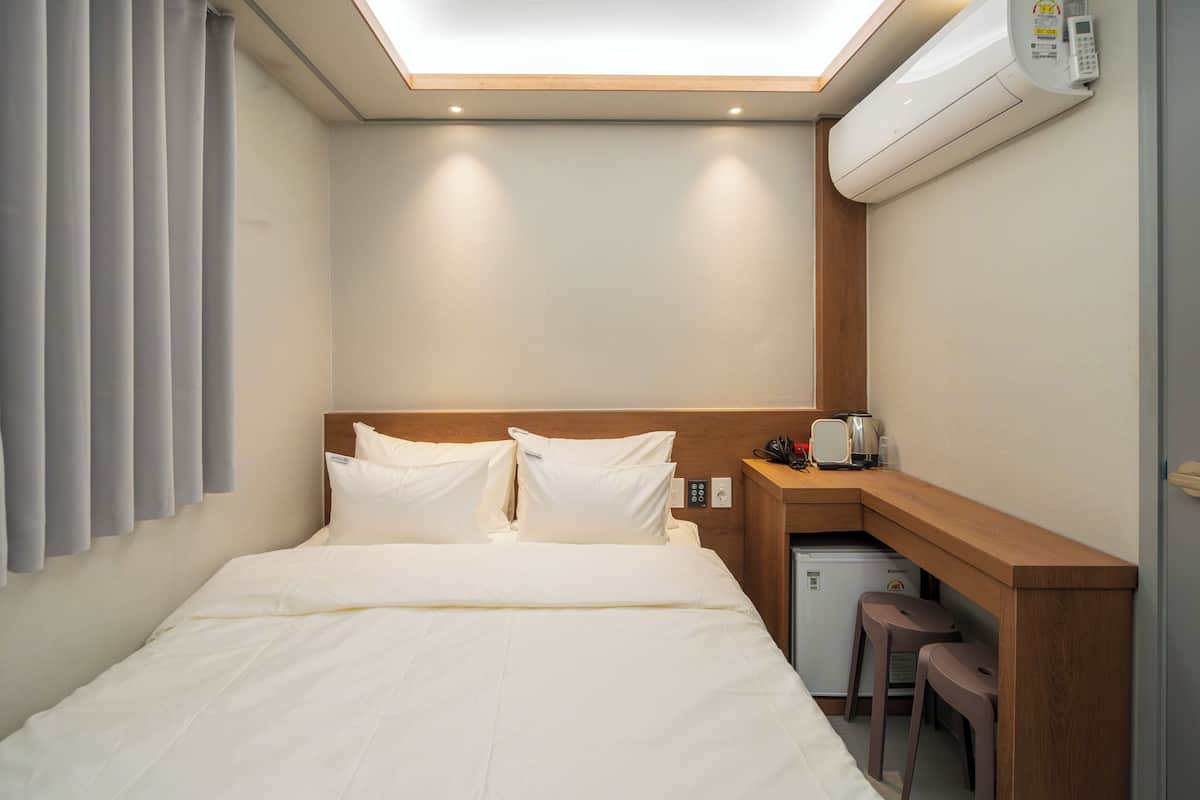 Une chambre d’hôtel équipée d’un lit, d’un bureau, d’un mini-réfrigérateur et d’un luminaire au plafond.
