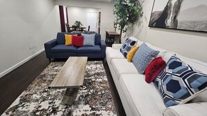 Ein Wohnzimmer mit einem blauen Sofa, einem weißen Sofa, einem Holztisch und einem gemusterten Teppich.