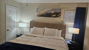 Ein ordentlich bezogenes Bett mit Kopfteil, einer Nachttischlampe, einem Nachttisch und einem Deckenventilator.
