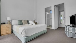 A modern hotel room with a bed, a TV, a desk, and a bathroom visible through an open door.